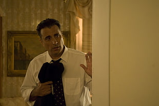 man in white dress shirt wearing black necktie holding black textile near wall